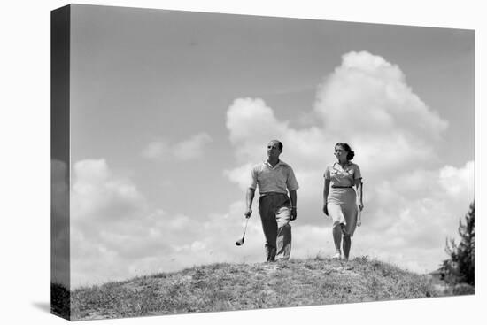 1930s COUPLE MAN WOMAN GOLFERS WALKING TOGETHER OVER CREST OF HILL CARRYING CLUBS-H. Armstrong Roberts-Premier Image Canvas