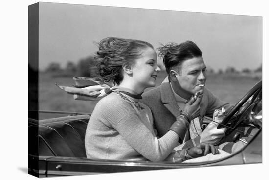 1930s MAN DRIVING CONVERTIBLE AUTOMOBILE WHILE GIRLFRIEND LIGHTS HIS CIGARETTE-H. Armstrong Roberts-Premier Image Canvas