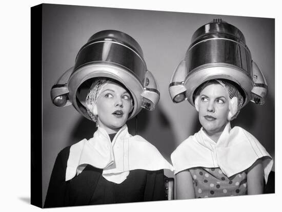 1950s TWO WOMEN SITTING UNDER BEAUTY SALON HAIR DRYERS WEARING HAIRNETS TOWELS TALKING GOSSIP-Panoramic Images-Premier Image Canvas