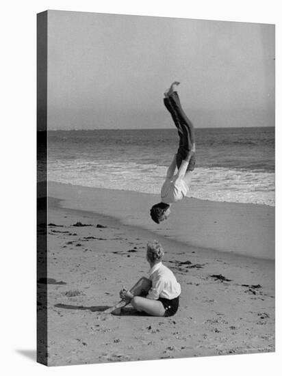Acrobat/Actor, Russ Tamblyn Doing a Flip on Beach with Movie Actress Venetia Stevenson Watching Him-Allan Grant-Premier Image Canvas