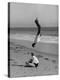 Acrobat/Actor, Russ Tamblyn Doing a Flip on Beach with Movie Actress Venetia Stevenson Watching Him-Allan Grant-Premier Image Canvas