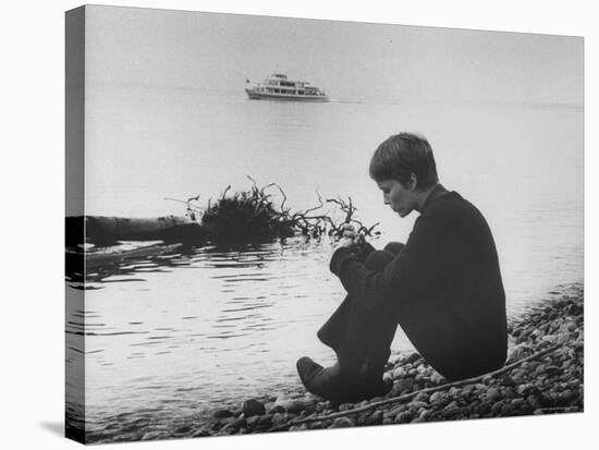 Actress Mia Farrow Pensively Sitting on Rocky Shore of Lake Geneva as Passenger Boat Passes By-Bill Eppridge-Premier Image Canvas