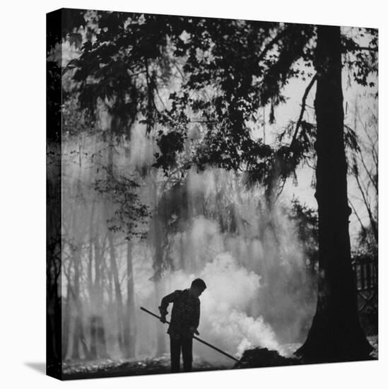 Boy Combining Play and Seasonal Chore, Stirring a Pile of Burning Leaves-Allan Grant-Premier Image Canvas