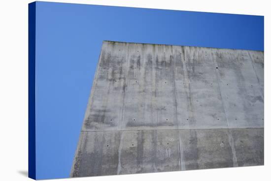 Concrete grey wall with structure and inclusions as a background in front of sky blue cloudless-Axel Killian-Stretched Canvas