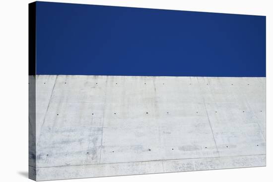 Concrete grey wall with structure and inclusions as a background in front of sky blue cloudless-Axel Killian-Stretched Canvas