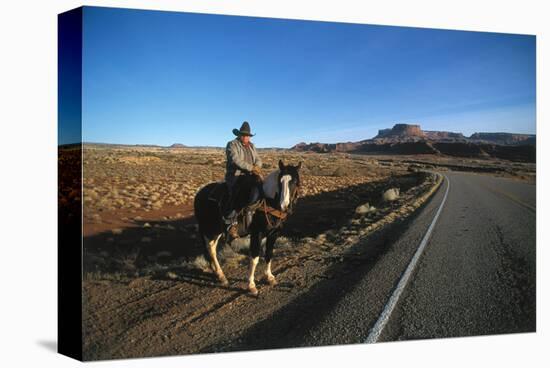 Cowboy on his horse on a highway near Hanksville, Utah, USA-null-Stretched Canvas