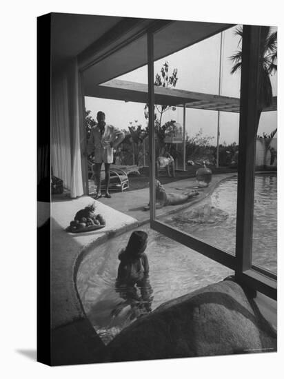 Designer Raymond Loewy Relaxing by Swimming Pool Which Runs from Outdoors Into Living Room-Peter Stackpole-Premier Image Canvas
