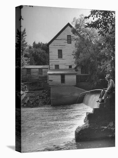 Man Fishing Beside a Waterfall and a 100 Year Old Mill-Bob Landry-Premier Image Canvas