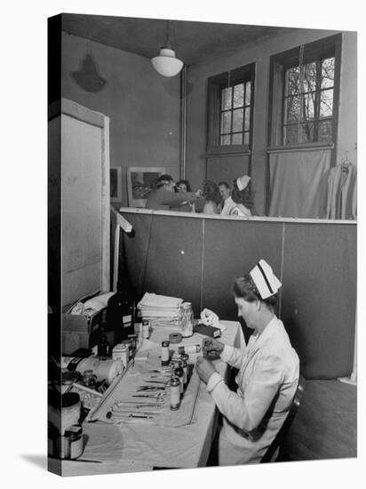 Nurse Sitting at Table with Medical Supplies While Doctors Examine Patient in Background-Wallace Kirkland-Premier Image Canvas