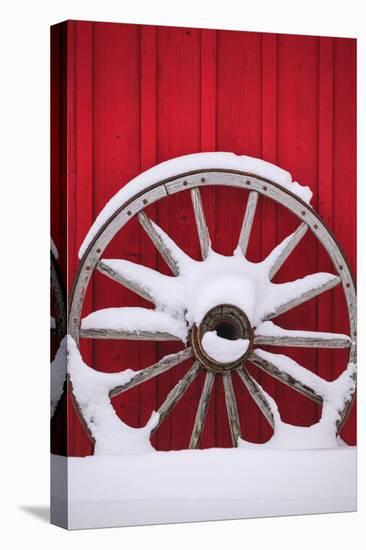 Snow-covered wagon wheels against red barn near town of Banff, Canadian Rockies, Alberta, Canada-Stuart Westmorland-Premier Image Canvas