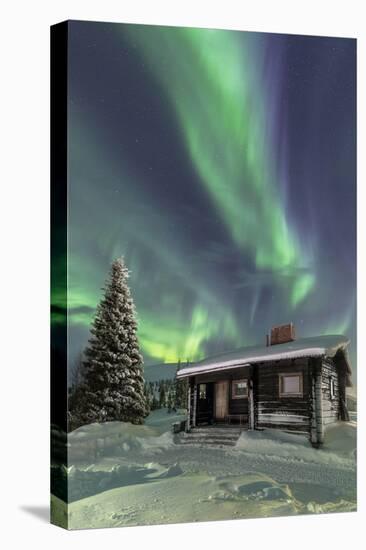 The Northern Lights (Aurora borealis) frame the wooden hut in the snowy woods, Pallas, Yllastunturi-Roberto Moiola-Premier Image Canvas