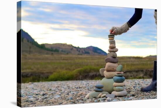 Woman Places A Final Rock Onto A Tall Rock Cairn-Hannah Dewey-Stretched Canvas