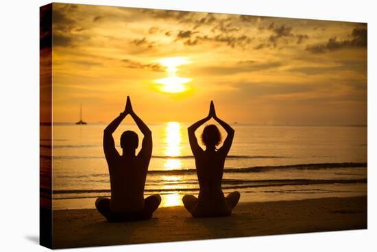 Young Couple Practicing Yoga On The Sea Beach At Sunset-De Visu-Stretched Canvas