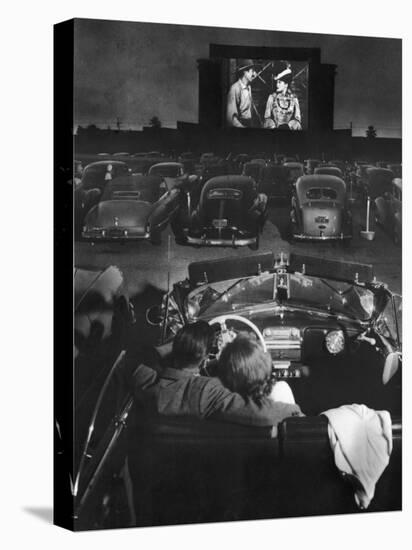 Young Couple Snuggling in Convertible as They Watch Large Screen Action at a Drive-In Movie Theater-J^ R^ Eyerman-Premier Image Canvas