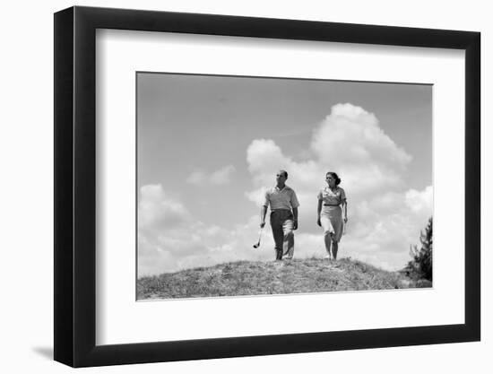 1930s COUPLE MAN WOMAN GOLFERS WALKING TOGETHER OVER CREST OF HILL CARRYING CLUBS-H. Armstrong Roberts-Framed Photographic Print