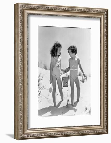 1930s TWO SMILING GIRLS SISTERS FRIENDS HOLDING HANDS AND SAND PAIL AND SHOVEL WALKING ON SAND DUNE-H. Armstrong Roberts-Framed Photographic Print