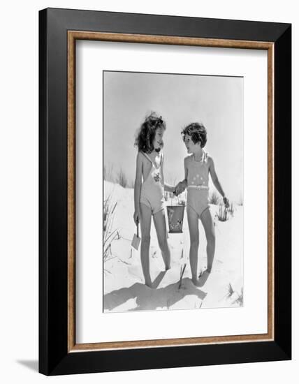 1930s TWO SMILING GIRLS SISTERS FRIENDS HOLDING HANDS AND SAND PAIL AND SHOVEL WALKING ON SAND DUNE-H. Armstrong Roberts-Framed Photographic Print