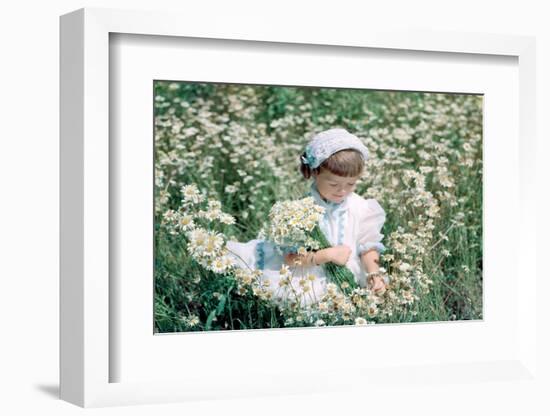 1950s 1960s LITTLE GIRL IN WHITE HAT AND DRESS PICKING WILDFLOWERS DAISES SITTING IN A WILD FLOW...-H. Armstrong Roberts-Framed Photographic Print