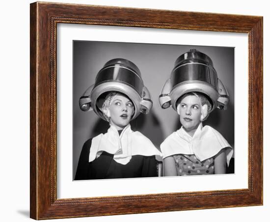1950s TWO WOMEN SITTING UNDER BEAUTY SALON HAIR DRYERS WEARING HAIRNETS TOWELS TALKING GOSSIP-Panoramic Images-Framed Photographic Print