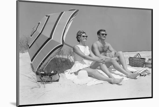 1960s COUPLE IN SUNGLASSES SITTING ON BEACH BLANKET WITH LEGS EXTENDED WITH UMBRELLA-H. Armstrong Roberts-Mounted Photographic Print