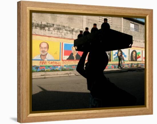 A Boy Carrying Bottles on His Head Passes by a Wall with Pictures of Haitian President Renel Preval-Ariana Cubillos-Framed Premier Image Canvas