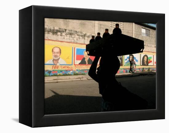 A Boy Carrying Bottles on His Head Passes by a Wall with Pictures of Haitian President Renel Preval-Ariana Cubillos-Framed Premier Image Canvas