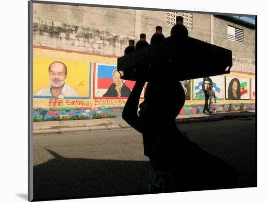 A Boy Carrying Bottles on His Head Passes by a Wall with Pictures of Haitian President Renel Preval-Ariana Cubillos-Mounted Photographic Print