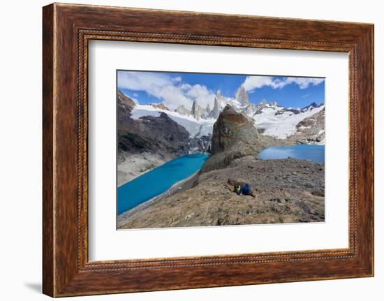 A couple in mountain gear rests on rocks with view to Lago de los Tres and Mount Fitz Roy, Patagoni-Fernando Carniel Machado-Framed Photographic Print