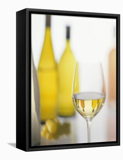 A Glass of White Wine and Wine Bottles in Background-Ulrike Koeb-Framed Premier Image Canvas