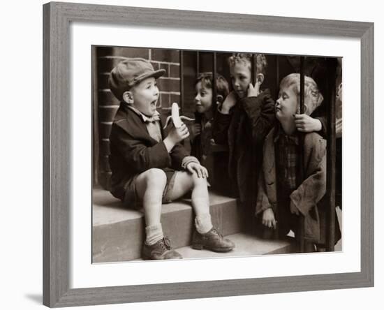 A Little Boy Holding a Banana Whilst Other Children Gaze Longingly at It-null-Framed Photographic Print