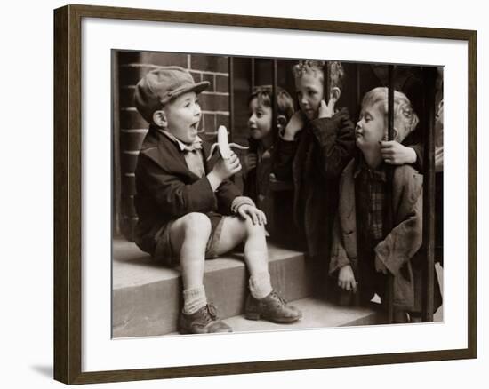 A Little Boy Holding a Banana Whilst Other Children Gaze Longingly at It-null-Framed Photographic Print