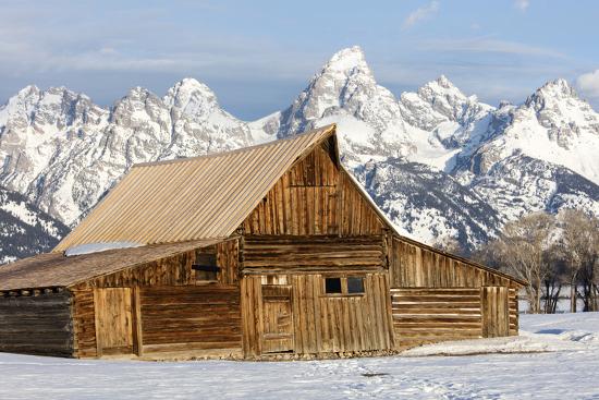 A Log Cabin Sits Before The Mass Of The Teton Range Photographic