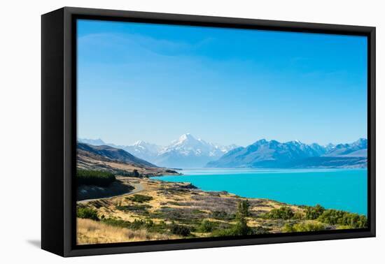 A road winds along the edge of a turquoise blue lake with mountains in the distance, New Zealand-Logan Brown-Framed Premier Image Canvas