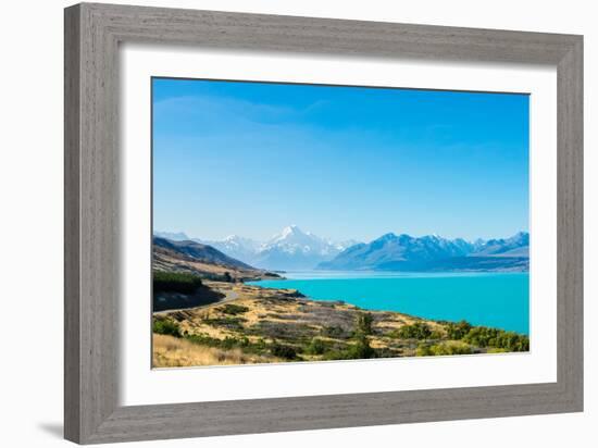 A road winds along the edge of a turquoise blue lake with mountains in the distance, New Zealand-Logan Brown-Framed Photographic Print