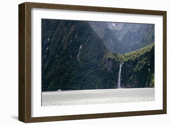 A sightseeing ship dwarfed by a tall waterfall in a fjord, South Island, New Zealand, Pacific-Logan Brown-Framed Photographic Print