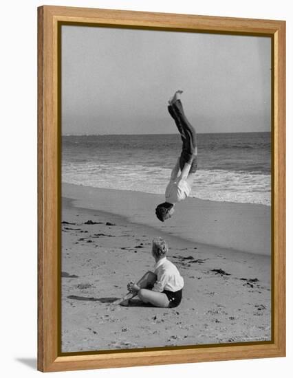 Acrobat/Actor, Russ Tamblyn Doing a Flip on Beach with Movie Actress Venetia Stevenson Watching Him-Allan Grant-Framed Premier Image Canvas