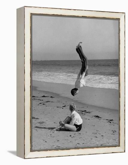 Acrobat/Actor, Russ Tamblyn Doing a Flip on Beach with Movie Actress Venetia Stevenson Watching Him-Allan Grant-Framed Premier Image Canvas