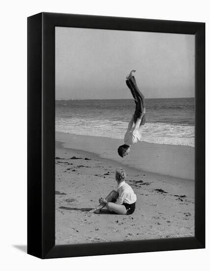 Acrobat/Actor, Russ Tamblyn Doing a Flip on Beach with Movie Actress Venetia Stevenson Watching Him-Allan Grant-Framed Premier Image Canvas