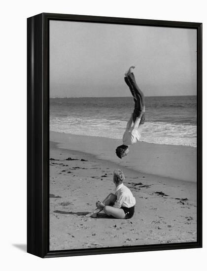 Acrobat/Actor, Russ Tamblyn Doing a Flip on Beach with Movie Actress Venetia Stevenson Watching Him-Allan Grant-Framed Premier Image Canvas