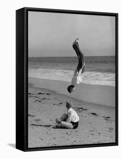 Acrobat/Actor, Russ Tamblyn Doing a Flip on Beach with Movie Actress Venetia Stevenson Watching Him-Allan Grant-Framed Premier Image Canvas