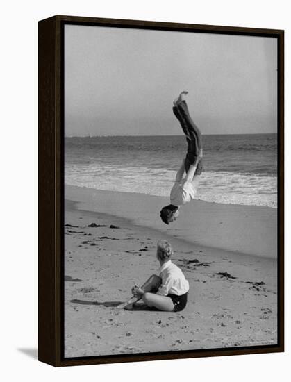 Acrobat/Actor, Russ Tamblyn Doing a Flip on Beach with Movie Actress Venetia Stevenson Watching Him-Allan Grant-Framed Premier Image Canvas