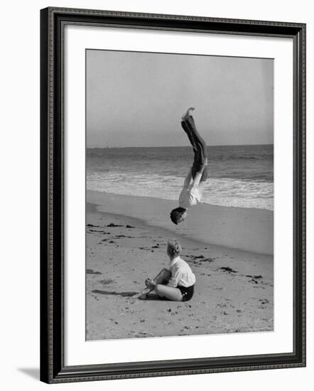 Acrobat/Actor, Russ Tamblyn Doing a Flip on Beach with Movie Actress Venetia Stevenson Watching Him-Allan Grant-Framed Premium Photographic Print