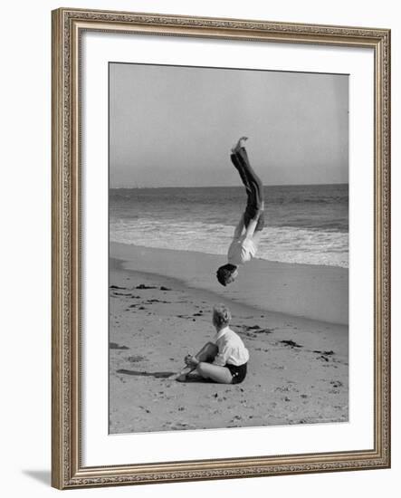 Acrobat/Actor, Russ Tamblyn Doing a Flip on Beach with Movie Actress Venetia Stevenson Watching Him-Allan Grant-Framed Premium Photographic Print