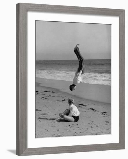 Acrobat/Actor, Russ Tamblyn Doing a Flip on Beach with Movie Actress Venetia Stevenson Watching Him-Allan Grant-Framed Premium Photographic Print