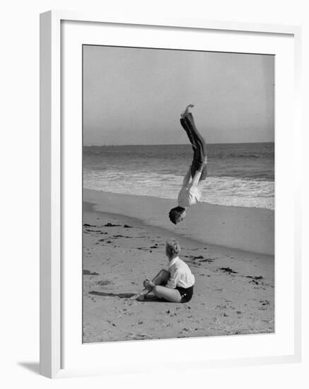 Acrobat/Actor, Russ Tamblyn Doing a Flip on Beach with Movie Actress Venetia Stevenson Watching Him-Allan Grant-Framed Premium Photographic Print