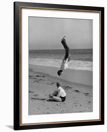 Acrobat/Actor, Russ Tamblyn Doing a Flip on Beach with Movie Actress Venetia Stevenson Watching Him-Allan Grant-Framed Premium Photographic Print