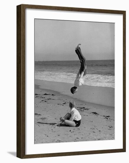 Acrobat/Actor, Russ Tamblyn Doing a Flip on Beach with Movie Actress Venetia Stevenson Watching Him-Allan Grant-Framed Premium Photographic Print