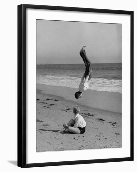 Acrobat/Actor, Russ Tamblyn Doing a Flip on Beach with Movie Actress Venetia Stevenson Watching Him-Allan Grant-Framed Premium Photographic Print