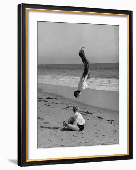 Acrobat/Actor, Russ Tamblyn Doing a Flip on Beach with Movie Actress Venetia Stevenson Watching Him-Allan Grant-Framed Premium Photographic Print