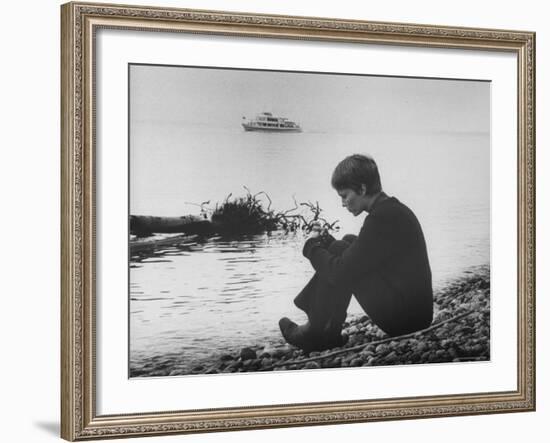 Actress Mia Farrow Pensively Sitting on Rocky Shore of Lake Geneva as Passenger Boat Passes By-Bill Eppridge-Framed Premium Photographic Print